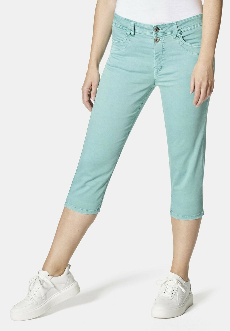 Helleblaue, taillierte, cropped Hose mit Reißverschluss und zwei Fronttaschen, kombiniert mit weißen Turnschuhen. Aus glattem Baumwollstoff.