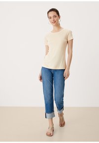 Jasnopestowy t-shirt z krótkim rękawem, połączony z niebieskimi dżinsami z podwiniętymi nogawkami i beżowymi sandałami. Gładki materiał z klasycznym okrągłym dekoltem.