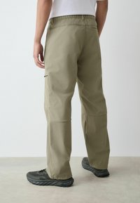 Kaki kravas bikses ar brīvu piegriezumu, elastīgu jostasvietu un sānu kabatām. Izgatavotas no gludas, vieglas auduma ar taisniem bikšu galiem.