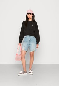 Felpa nera corta con logo, pantaloni corti usurati azzurri, cappellino rosa, borsa trasparente rosa e sneakers con stampa leopardata multicolore.