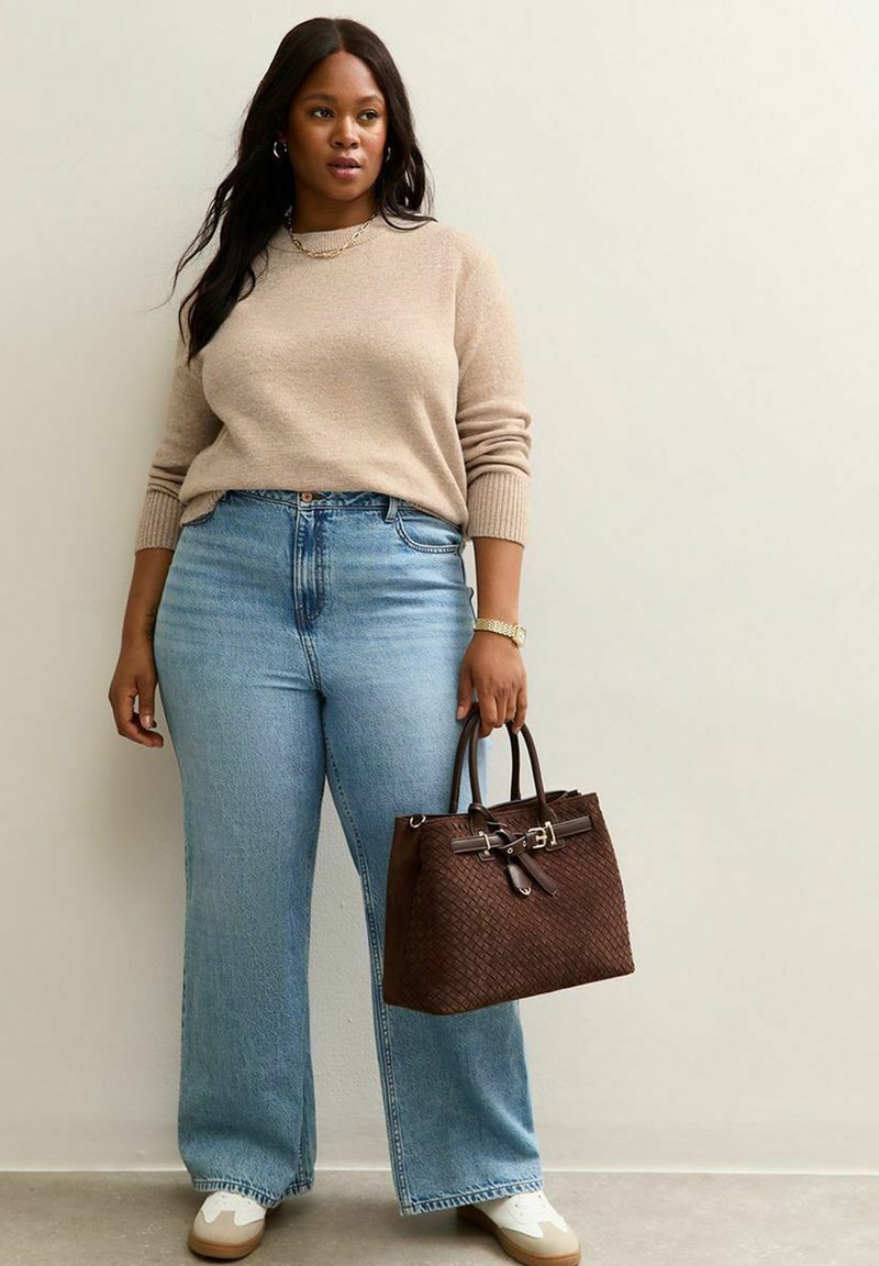 Brązowy sweter, jasnoniebieskie dżinsy z wysokim stanem, brązowa pleciona torebka, białe trampki. Bransoletka i naszyjnik jako dodatki, długie ciemne włosy.