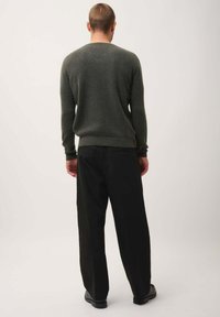 Donkergroene gebreide trui met een ronde hals, gecombineerd met zwarte losvallende broek en zwarte schoenen. Minimalistische stijl, geen zichtbare patronen.