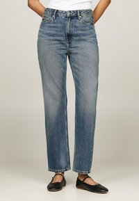 Vaqueros azules de talle alto con diseño de pierna recta, que cuentan con cinco bolsillos, sutiles decoloraciones y costuras en contraste. Combinados con zapatos planos negros.