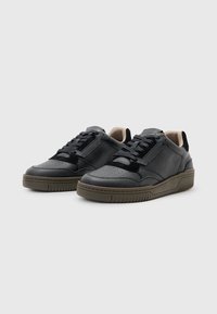 Sneaker nere in pelle con finitura texturizzata, dotate di perforazioni sulla punta, allacciatura tono su tono e suola in gomma verde scuro.