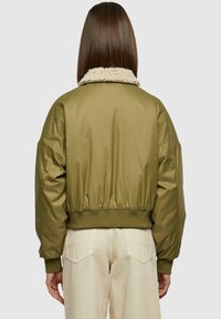 Giacca bomber verde oliva con colletto in finta pelliccia testurizzata, polsini e orlo a coste. Maniche imbottite che si restringono verso il polso.