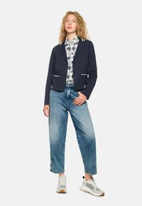 Navy cropped blazer with white accents, paired with a patterned shirt and light blue baggy jeans. Footwear includes gray and white sneakers.