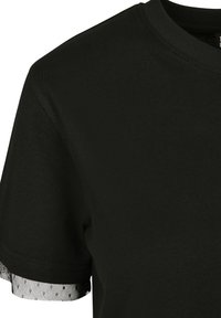 Cămașă neagră cu mâneci scurte, decolteu rotund și material negru tip plasă vizibil, care se extinde ușor dincolo de marginea mânecii.