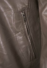 Brown leather jacket with a textured finish, featuring a zippered pocket on the left side and contrasting stitching along the seams.
