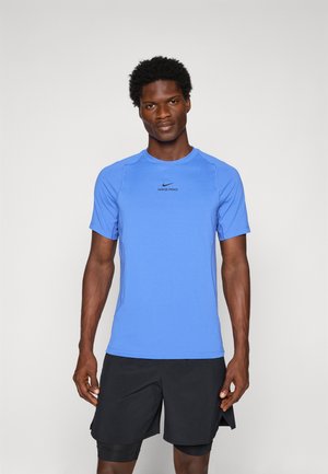 Hombre atlético de pie, vistiendo una camiseta azul de manga corta Nike Pro y pantalones cortos negros de capas, mirando de frente contra un fondo neutro.