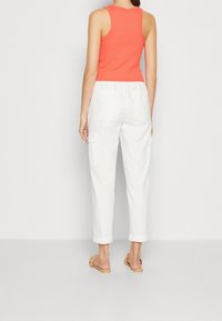 Koraalrode mouwloze ribtop met witte cargo broeken, uitgerust met een elastische tailleband en zijzakken. Simpele sandalen maken de look compleet.