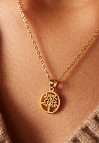 Gouden levensboom hanger aan een dunne gouden ketting. De hanger heeft een gedetailleerd boomontwerp binnen een ronde omlijsting.