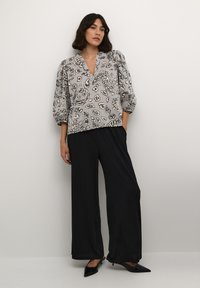Blusa grigia con stampa leopardata, scollatura a V e maniche a palloncino, abbinata a pantaloni neri a gamba larga e décolleté neri a punta.