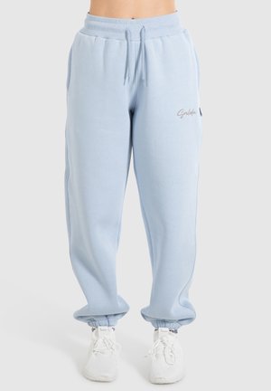 Lichtblauwe sweatpants met elastische manchetten en een taillekoord, gedragen met witte sportschoenen door een staande persoon.
