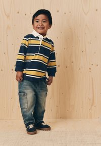 Polo rayé bleu et jaune avec un col blanc, accompagné d'un pantalon cargo en denim bleu clair et de baskets foncées à lacets blancs.