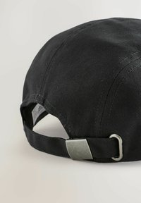 Sort kasket med en struktureret design, har et tekstureret stof, justerbar rem med en metalspænde, og syninger langs sømmene.
