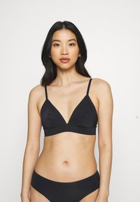 Bralette preto em forma de triângulo com alças finas ajustáveis, tecido macio e detalhes de costura. Combinado com um soutien de bikini preto correspondente.