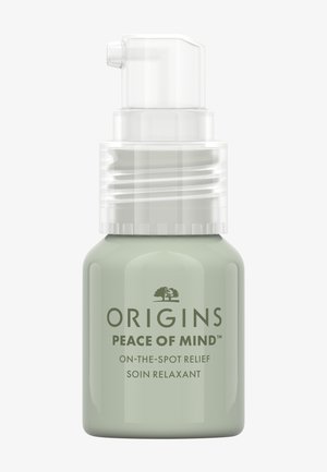 Groene glazen fles met een pompdispenser. Label met de tekst "Origins Peace of Mind" in donkere letters. Gladde textuur, minimalistisch ontwerp.