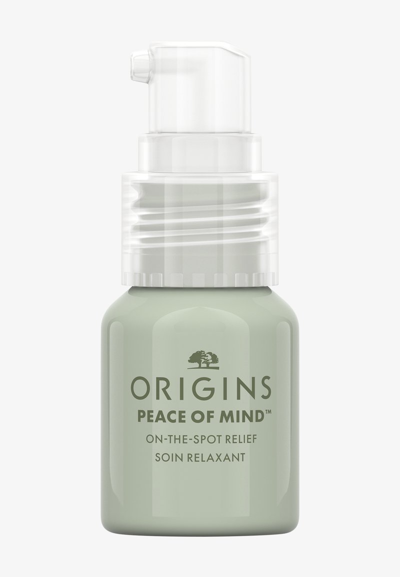 Vihreä lasipullo, jossa on pumppupumppu. Labelissa teksti "Origins Peace of Mind" tummalla tekstillä. Sileä pinta, minimalistinen muotoilu.