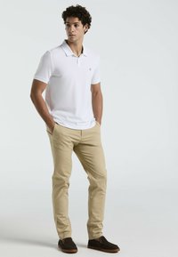 Witte polo met korte mouwen, beige slim-fit broek, bruine instap schoenen, casual kleding met een eenvoudig ontwerp en zonder zichtbare patronen.