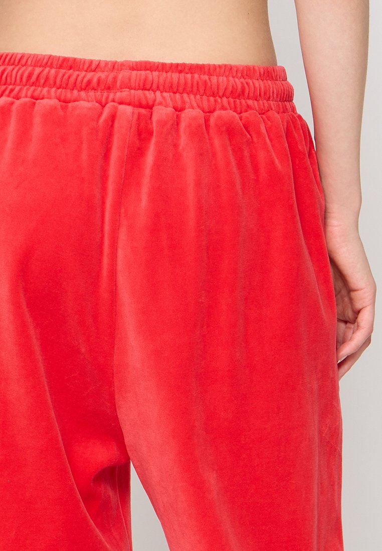 Rote Samt-Jogginghosen mit weicher Textur, elastischem Bund und r gathered ankle cuffs. Glatte Oberfläche und lebendige Farbe.