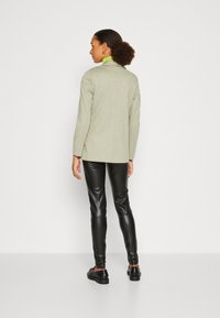 Ljust grön blazer med långa ärmar, detalj på bakseam, kombinerad med svarta konstläderbyxor och svarta platta skor, minimalistisk design.