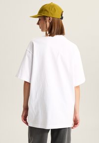 Hvid oversized t-shirt med korte ærmer, lavet af bomuldsstof. Sammen med en sennepsgul kasket med buet skygge og justerbar rem.
