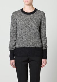Pull tricoté avec un corps gris texturé et un ourlet ainsi que des poignets noirs et duveteux. Il présente un col rond et des manches longues.