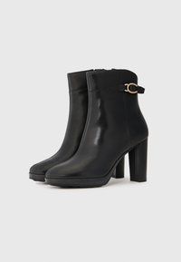 Svarta läderankelboots med en slät finish, med en hög klack i blockform och en guldtonad spänneaccent på sidan.