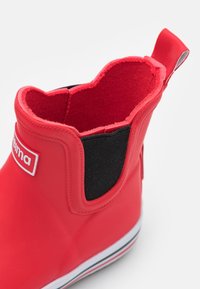 Botte de pluie en caoutchouc rouge pour enfant avec panneau latéral élastique noir, tirant à l'arrière et semelle blanche avec des rayures rouges et noires.