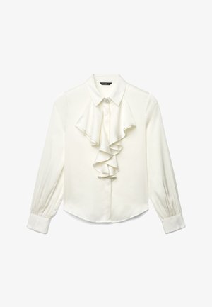 Blouse blanche à manches longues avec col pointu, détail à volants à l'avant et broche décorative au niveau du col.