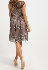 Krátký rukáv, šaty po kolena z průhledné hnědé látky, s stříbrným květinovým vyšíváním a přiléhavým pasem, doplněné o nahé lodičky.