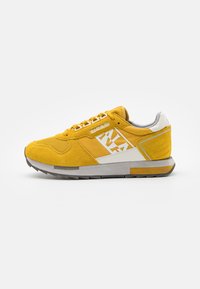 Sneakers in suede giallo con accenti bianchi, dotati di una parte superiore testurizzata, lacci sottili e suola in gomma grigia. Dettaglio del logo laterale visibile.
