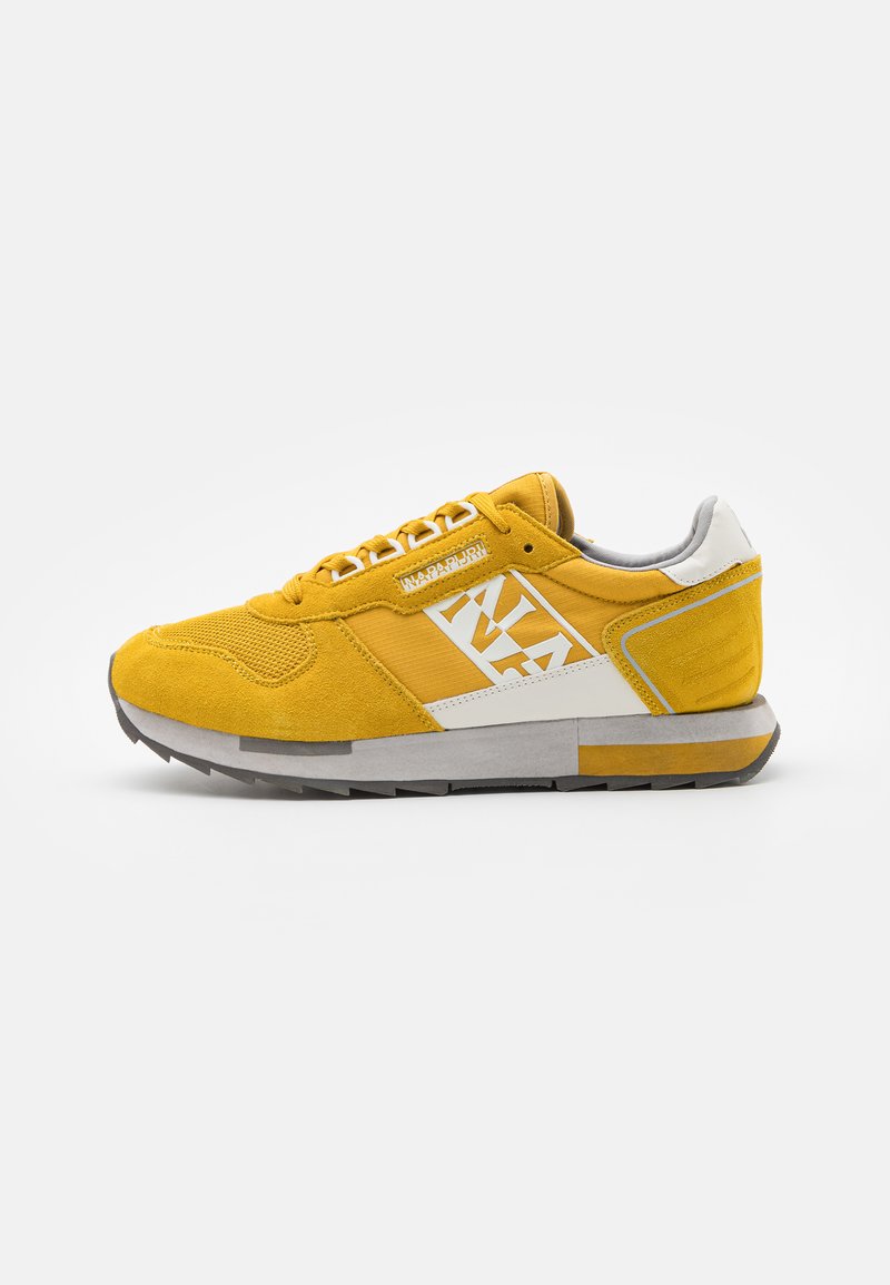 Sneakers in suede giallo con accenti bianchi, dotati di una parte superiore testurizzata, lacci sottili e suola in gomma grigia. Dettaglio del logo laterale visibile.