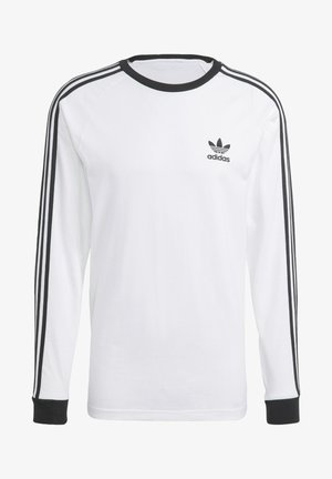 Maglietta a maniche lunghe in cotone bianco con dettagli neri, caratterizzata da un collo rotondo e un design a tre strisce nere lungo le maniche. Logo Adidas.