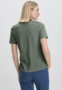 Vihreä lyhythihainen t-paita, joka on valmistettu pehmeästä puuvillasta ja jossa on pyöreä kaulus. Omistaa rentoa istuvuutta ja hienovaraista tekstuuria, yhdistettynä sinisiin housuihin.