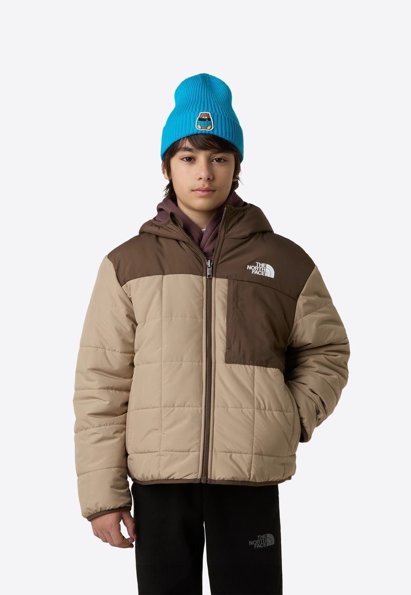 Obložena jakna v bež in rjavi barvi z zadrgo, kapuco in sprednjim žepom. Kombinirana z modro rebrasto pleteno kapo.