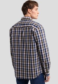Camisa de cuadros en tonos azul oscuro, verde y blanco. Mangas largas y cuello con botones, con un detalle de yugo en la parte posterior. Tejido texturizado.
