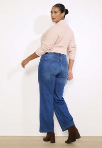 Kõrge vöökoht ja lõdva lõikega sinised teksad, millel on taga taskud ja peened õmbluse detailid, koos heleda roosa sviitriga.