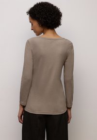 Top beige a maniche lunghe realizzato in materiale morbido, con scollo rotondo e silhouette aderente, abbinato a pantaloni scuri con trama.