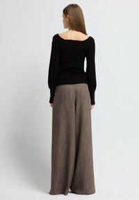 Schwarzer gerippter Pullover mit weitem Halsausschnitt, kombiniert mit weiten, strukturierten braunen Hosen, die ein subtile Muster aufweisen.