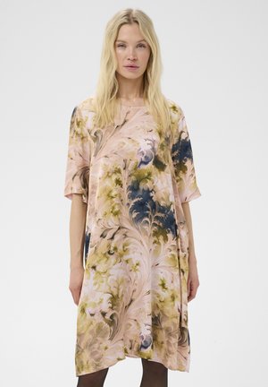 Femme blonde portant une robe ample mi-longue à manches courtes avec un motif floral tourbillonnant en tons rose, vert et marine.