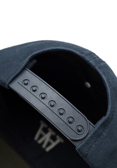 Cappellino blu navy con tessuto testurizzato e una striscia regolabile in plastica dotata di fori circolari e bottoni per le regolazioni della misura.