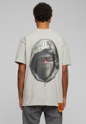 Grå bomulds t-shirt med et stort grafisk motiv af en maskeret figur med en lynlåsdetalje. Indeholder et orange stofmærke i kanten.