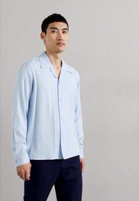 Lichtblauw overhemd met lange mouwen, gemaakt van gladde stof, met een gespreide kraag en eenvoudige knoppenmanchetten, gecombineerd met donkere broek.