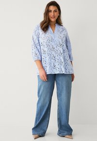 Hellbluse mit Stickerei, V-Ausschnitt und Dreiviertelärmeln, filigranen Ausstanzungen, kombiniert mit blauen weiten Jeans.