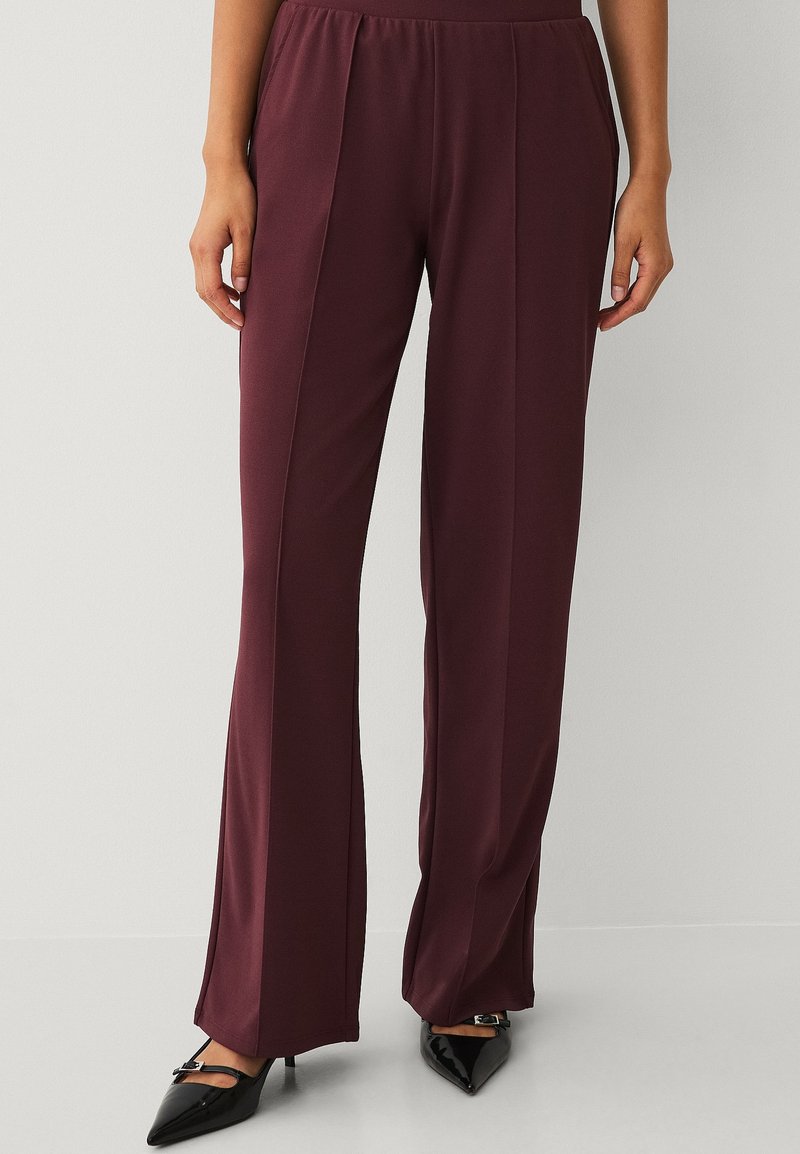 Pantalones de pierna ancha color granate hechos de material elástico, con una textura lisa, cintura elástica y pliegues verticales para una alineación estructurada.