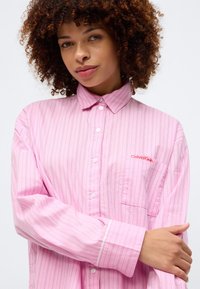 Ροδοκόκκινη ριγέ πουκάμισο με κοντό γιακά, ενιαία τσέπη στο στήθος και κόκκινο λογότυπο "Calvin Klein". Μαλακό, ελαφρύ ύφασμα με χαλαρή εφαρμογή.