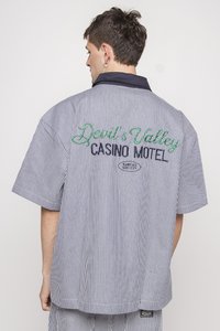 Short-sleeve, striped shirt in navy and white cotton. Features embroidered text: "Devil's Valley Casino Motel" in green and navy.