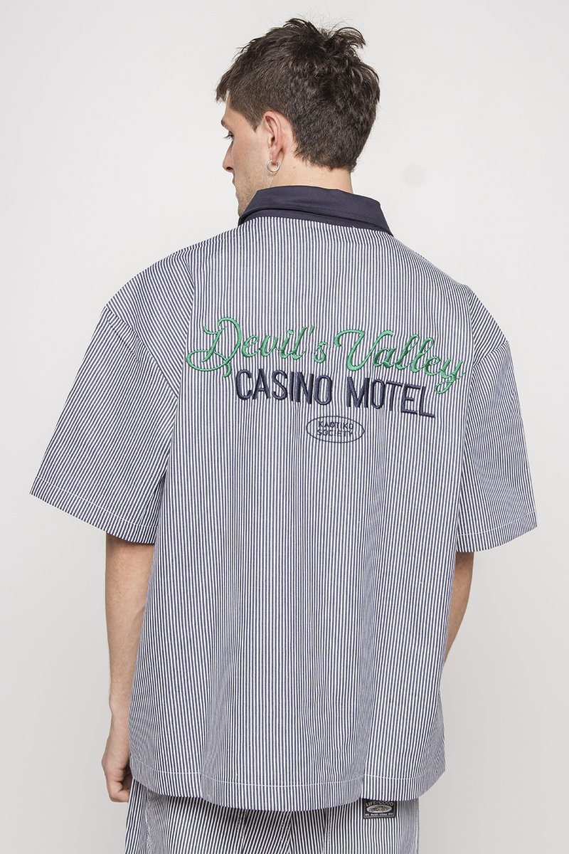 Short-sleeve, striped shirt in navy and white cotton. Features embroidered text: "Devil's Valley Casino Motel" in green and navy.