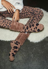 Braune Leopardenmuster-Socken mit einer weichen, flauschigen Textur und einem umgeschlagenen Design. Tragen Sie sie mit passenden gemusterten Leggings auf einer sanften Oberfläche.
